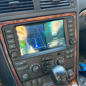 Car infotainment screen showing Apple CarPlay map on left and a music widget on right in a car with wood trim dashboard